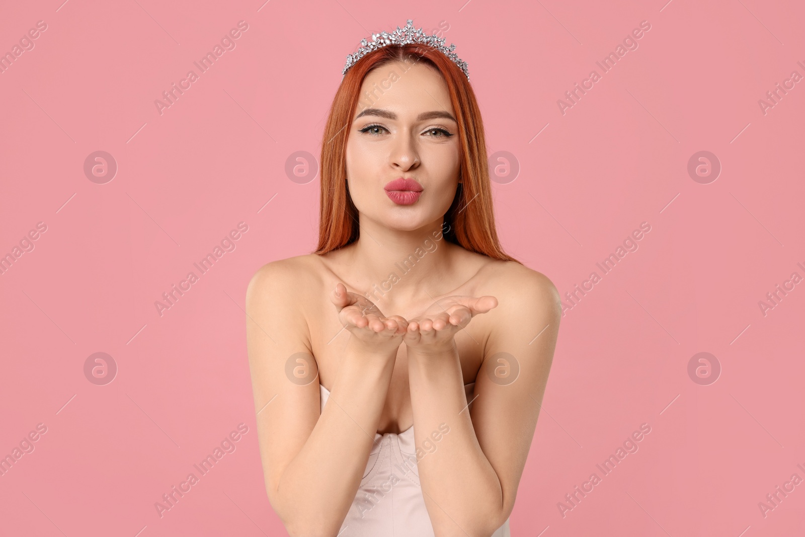 Photo of Beautiful young woman with tiara blowing kiss on pink background