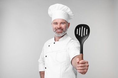 Photo of Happy chef in uniform with spatula on grey background