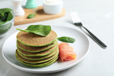 Tasty spinach pancakes with salmon on light grey table, closeup