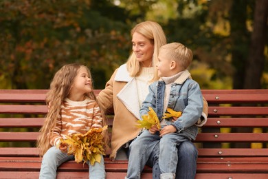 Photo of Happy mother and her children spending time together with dry leaves in autumn park