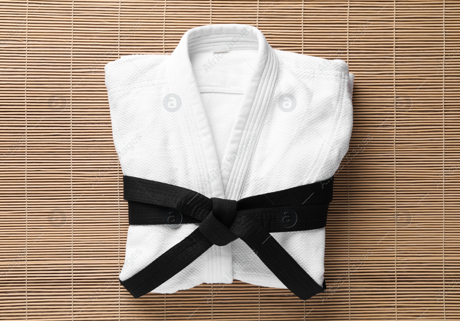 Photo of Martial arts uniform with black belt on bamboo mat, top view