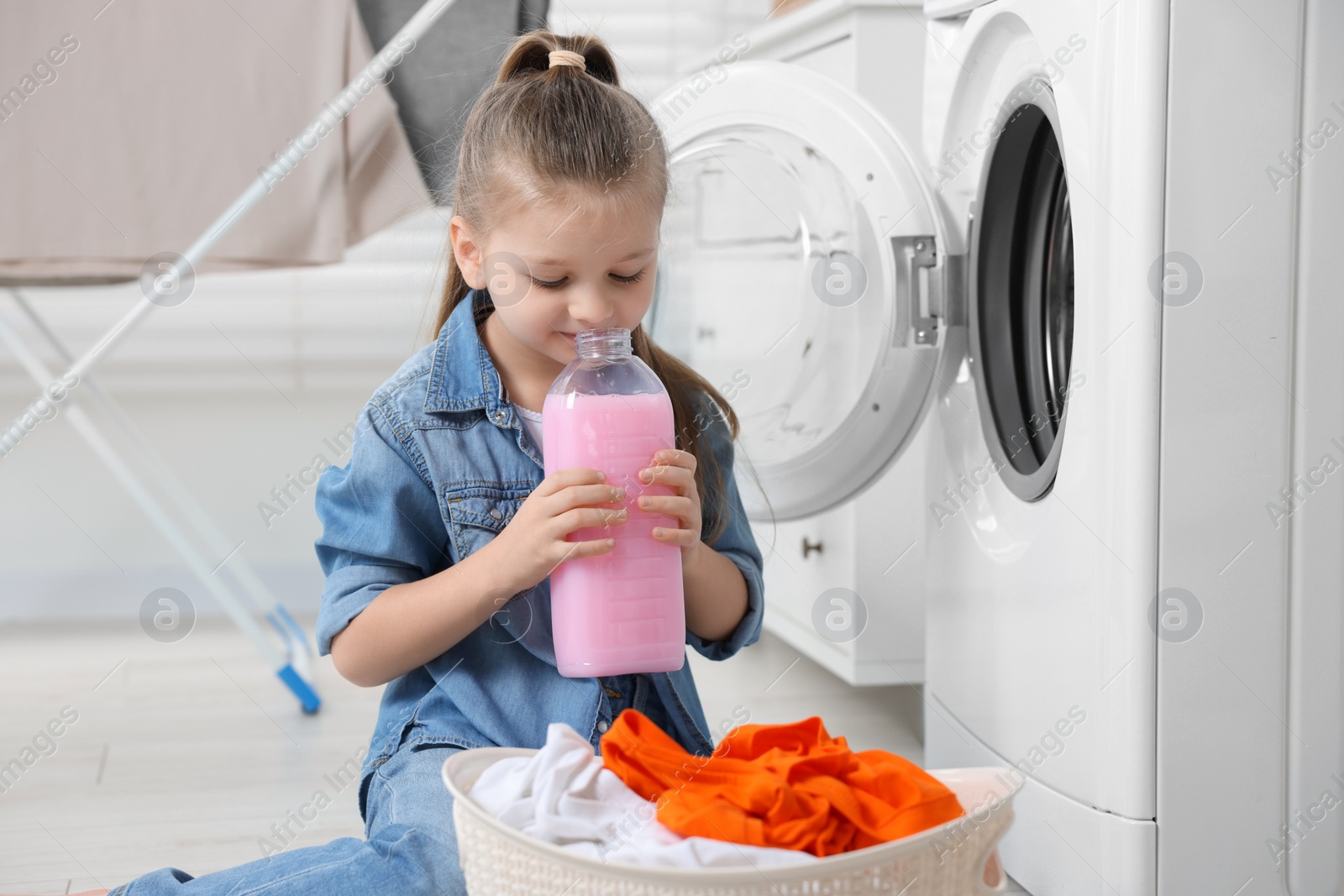 Photo of Little girl smelling fabric softener in bathroom