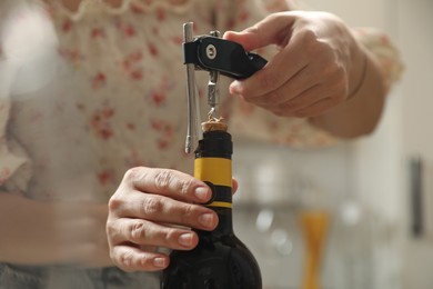 Woman opening wine bottle with corkscrew on blurred background, closeup