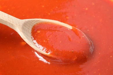 Photo of Wooden spoon in tasty tomato sauce, closeup