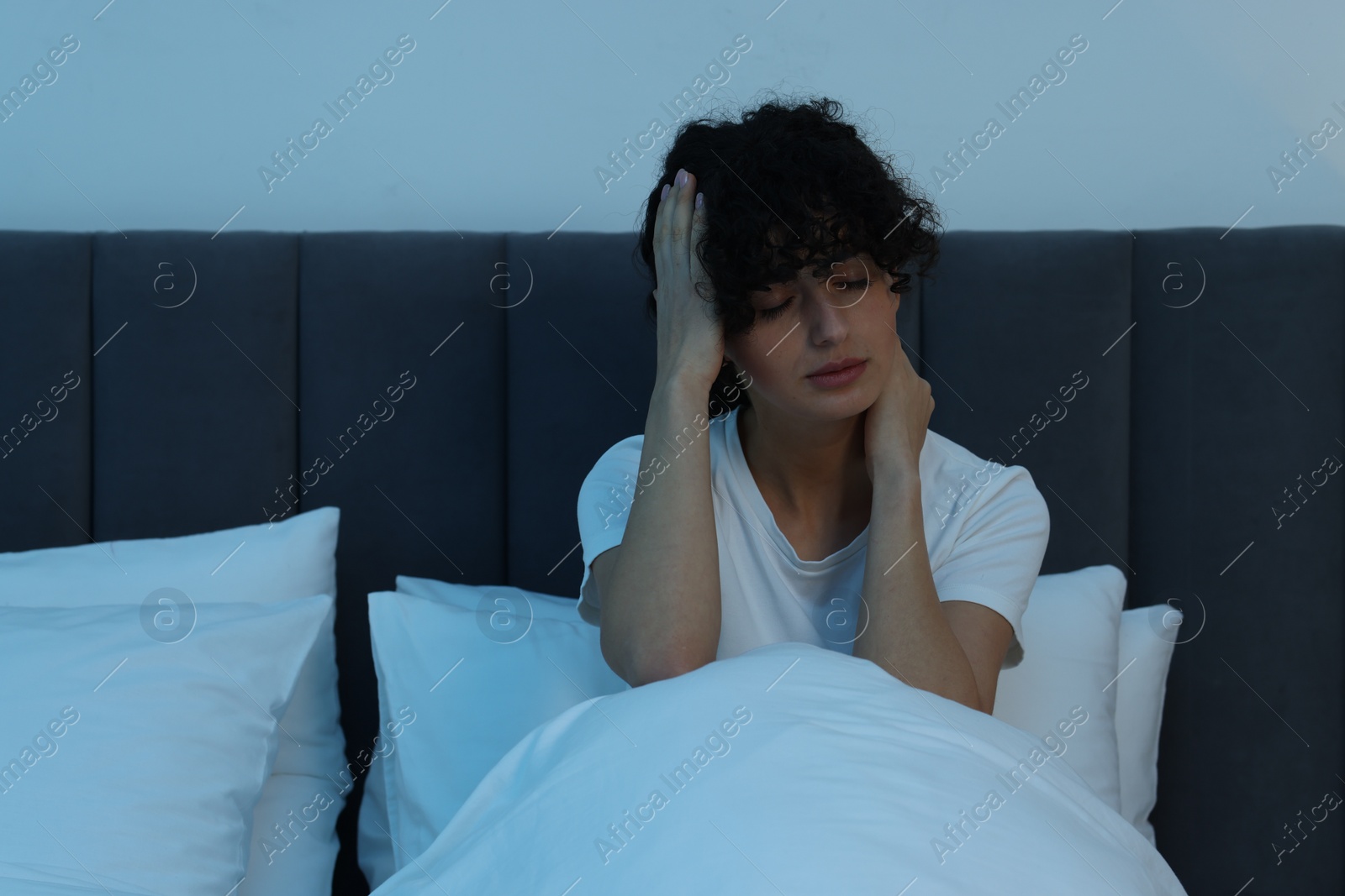 Photo of Young woman suffering from headache in bed at night