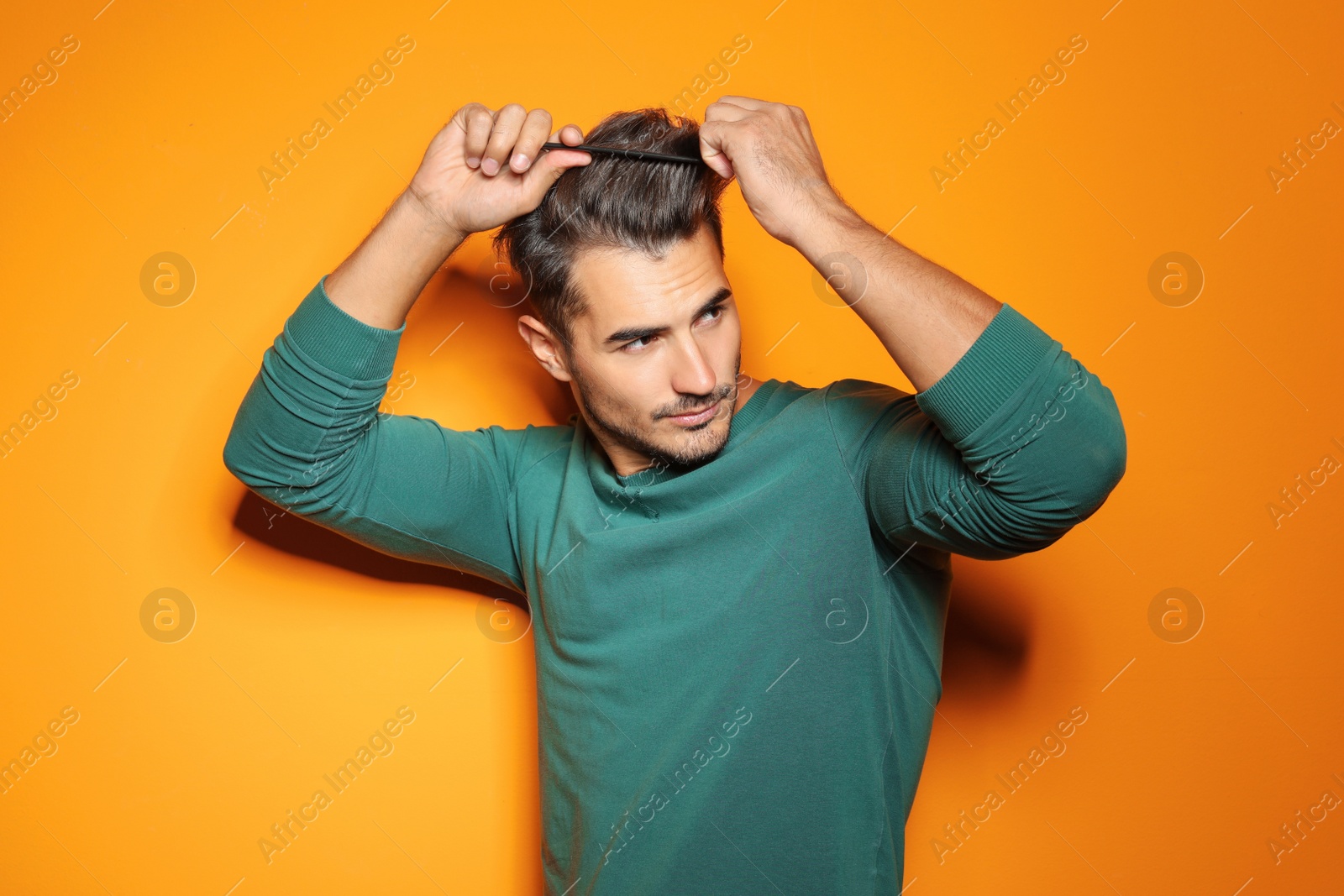 Photo of Young man with comb posing on color background. Trendy hairstyle