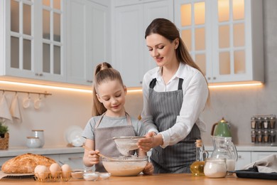 Photo of Making bread. Mother and her daughter preparing dough in bowl at wooden table in kitchen