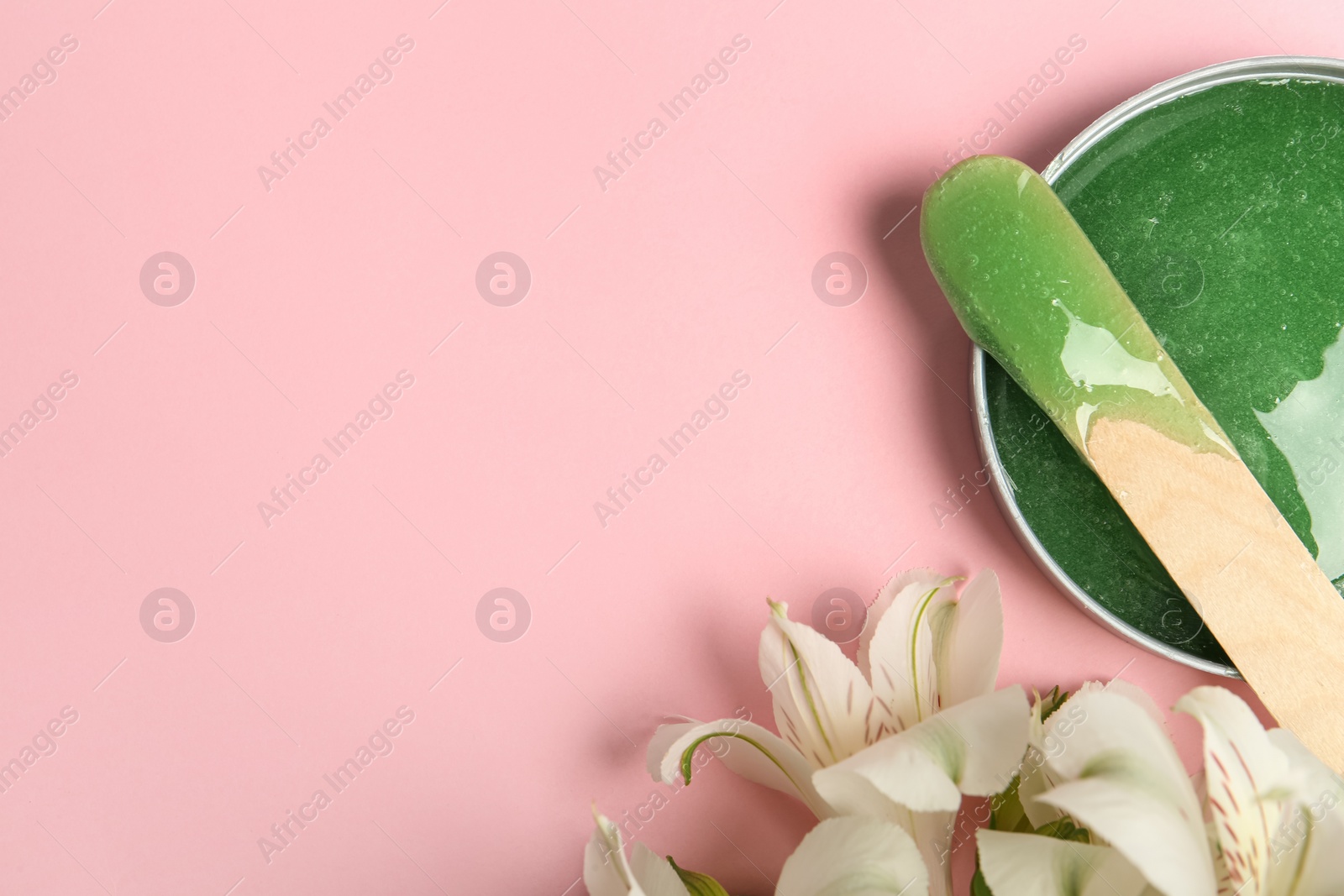 Photo of Wooden spatula, hot depilatory wax and flowers on light pink background, flat lay. Space for text