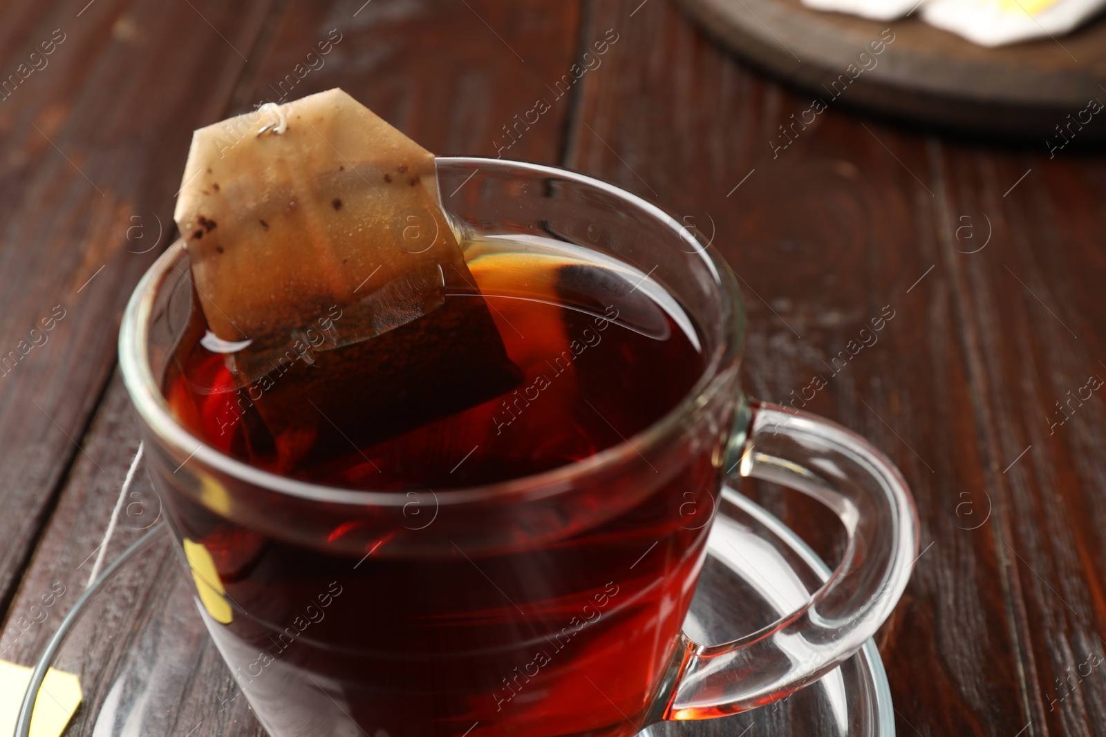 Photo of Brewing tea. Glass cup with tea bag on wooden table, closeup