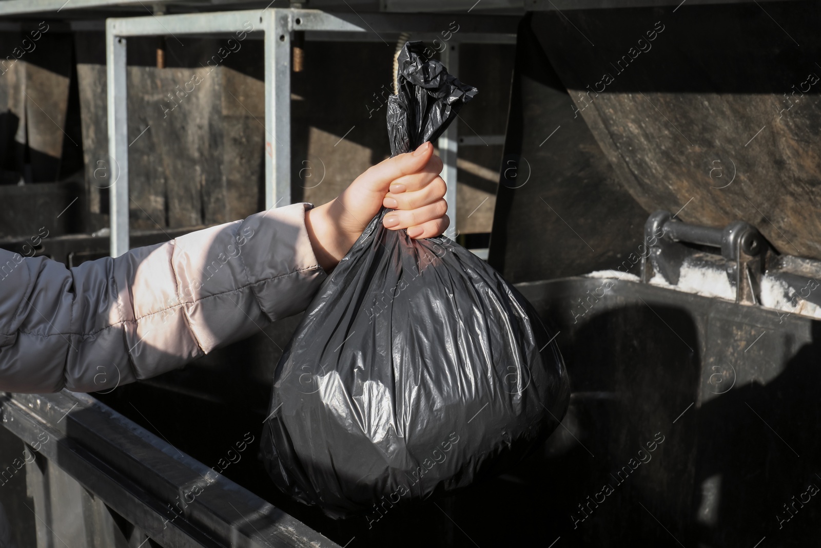 Photo of Woman throwing trash bag full of garbage in bin outdoors, closeup