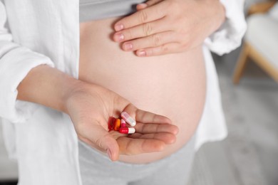 Photo of Pregnant woman holding pile of pills indoors, closeup