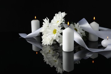 Photo of White chrysanthemum flowers and burning candles on black mirror surface in darkness, space for text. Funeral symbols