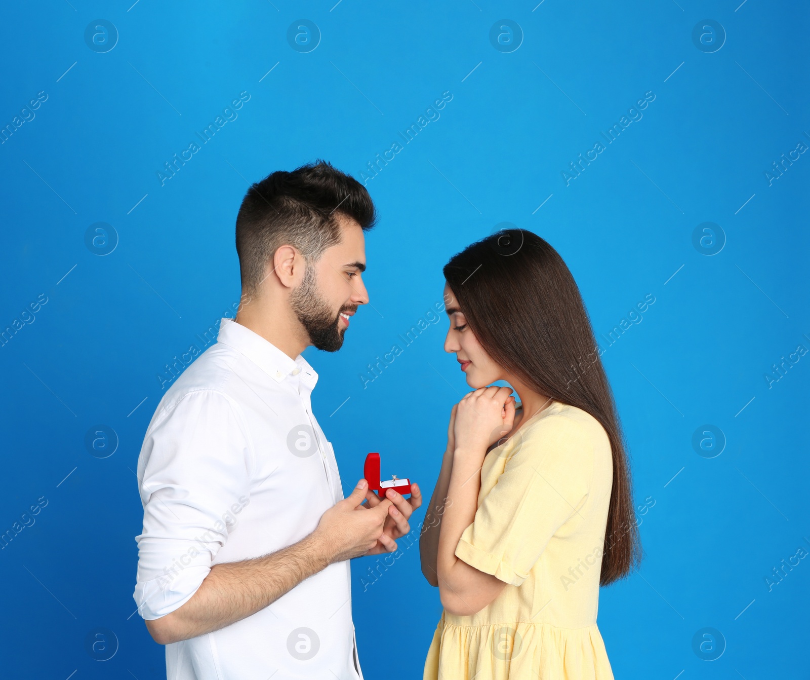 Photo of Man with engagement ring making marriage proposal to girlfriend on blue background