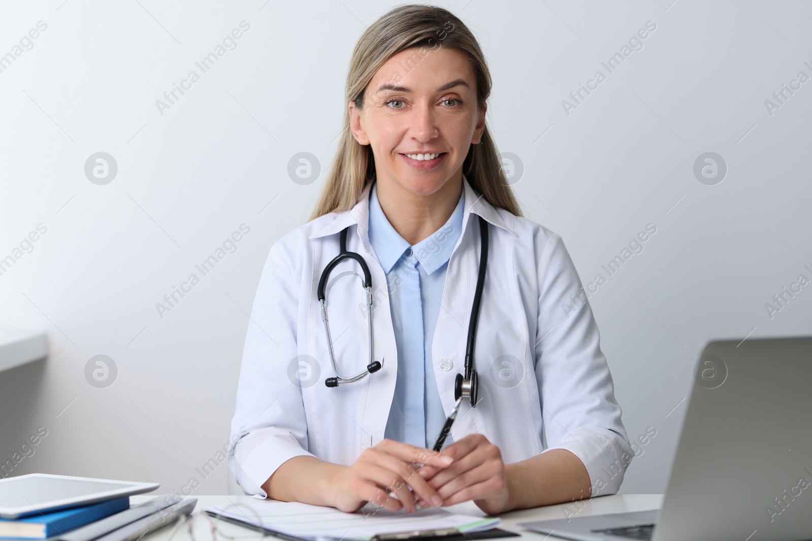 Photo of Portrait of happy doctor with stethoscope at white table in hospital