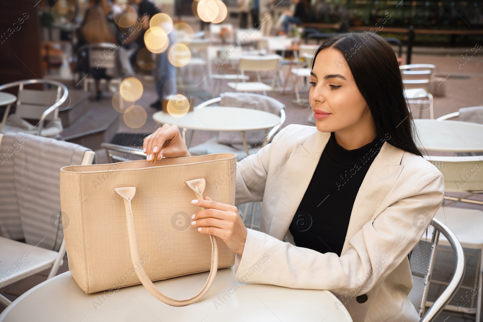 Photo of Young woman with stylish bag at table in outdoor cafe