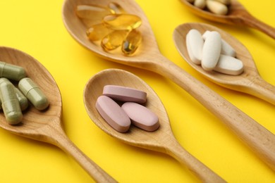 Photo of Different vitamin pills in spoons on yellow background, closeup