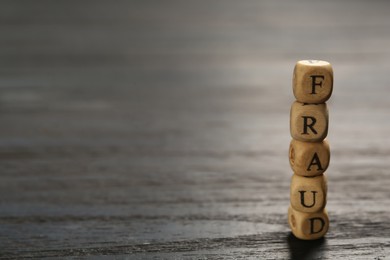 Photo of Word Fraud of cubes with letters on black wooden background. Space for text