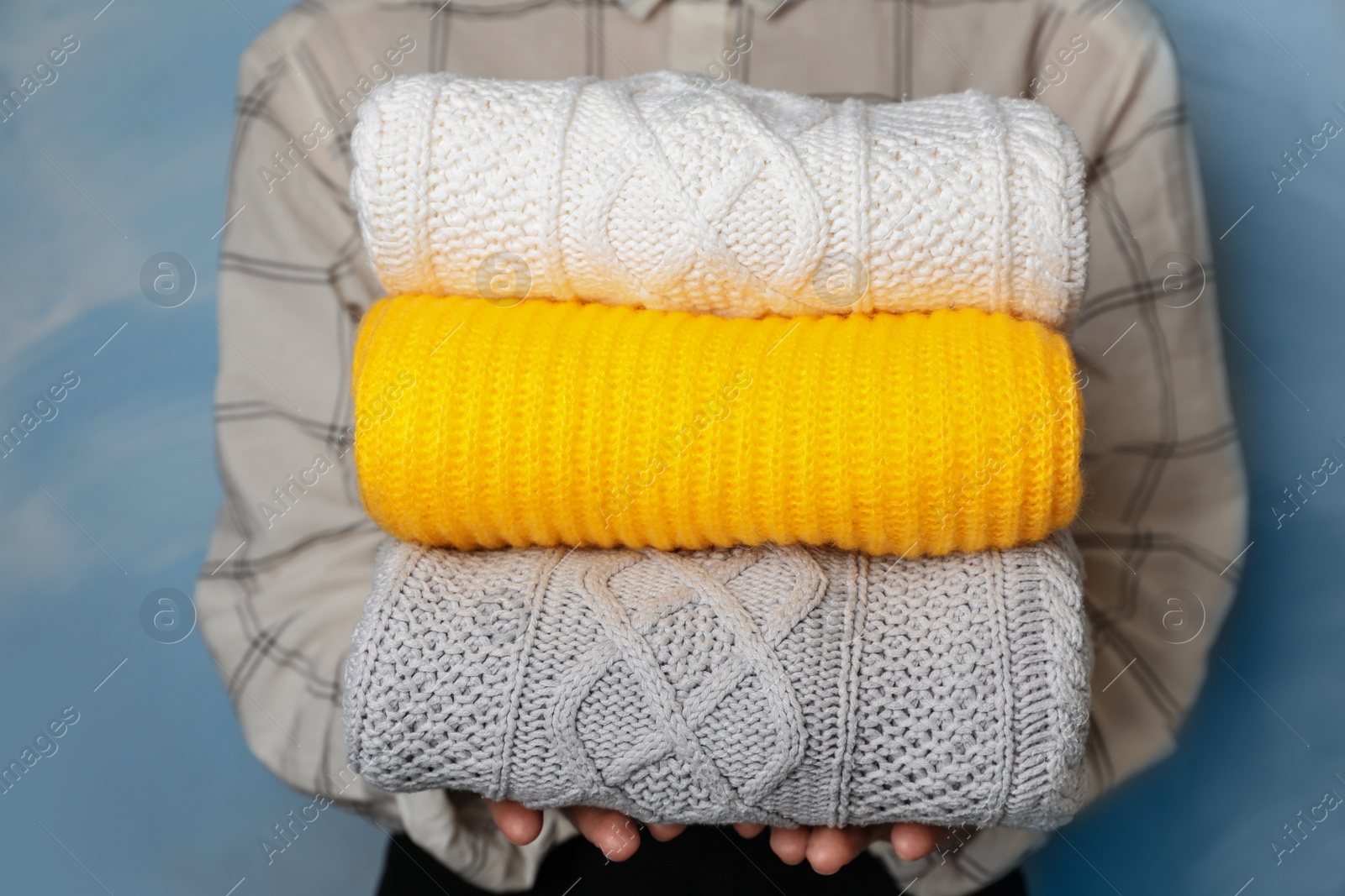 Photo of Woman holding stack of folded warm knitted sweaters, closeup