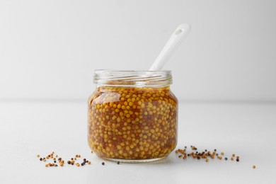 Photo of Whole grain mustard in jar and dry seeds on white table