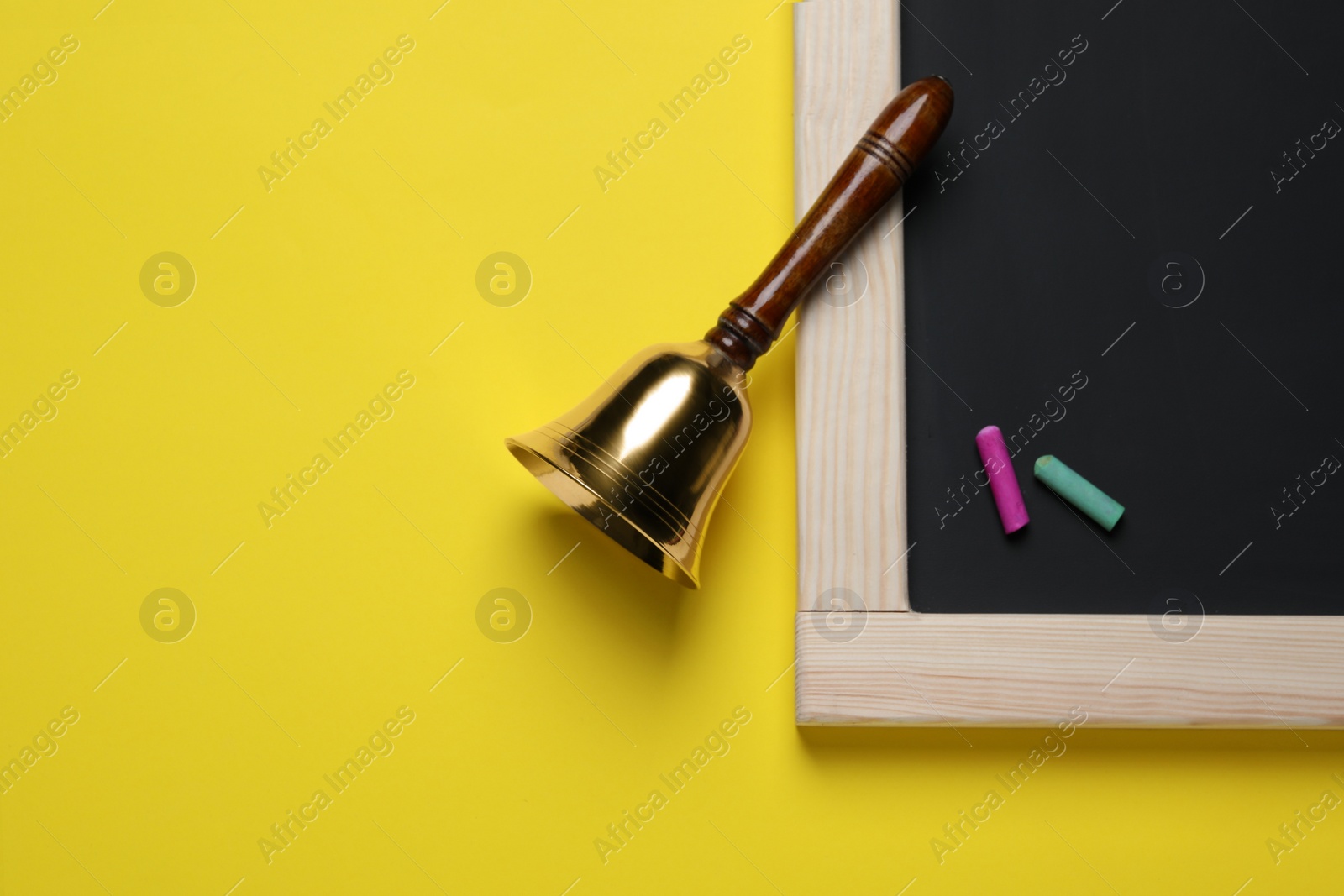 Photo of Golden bell, blackboard and pieces of chalk on yellow background, flat lay. School days