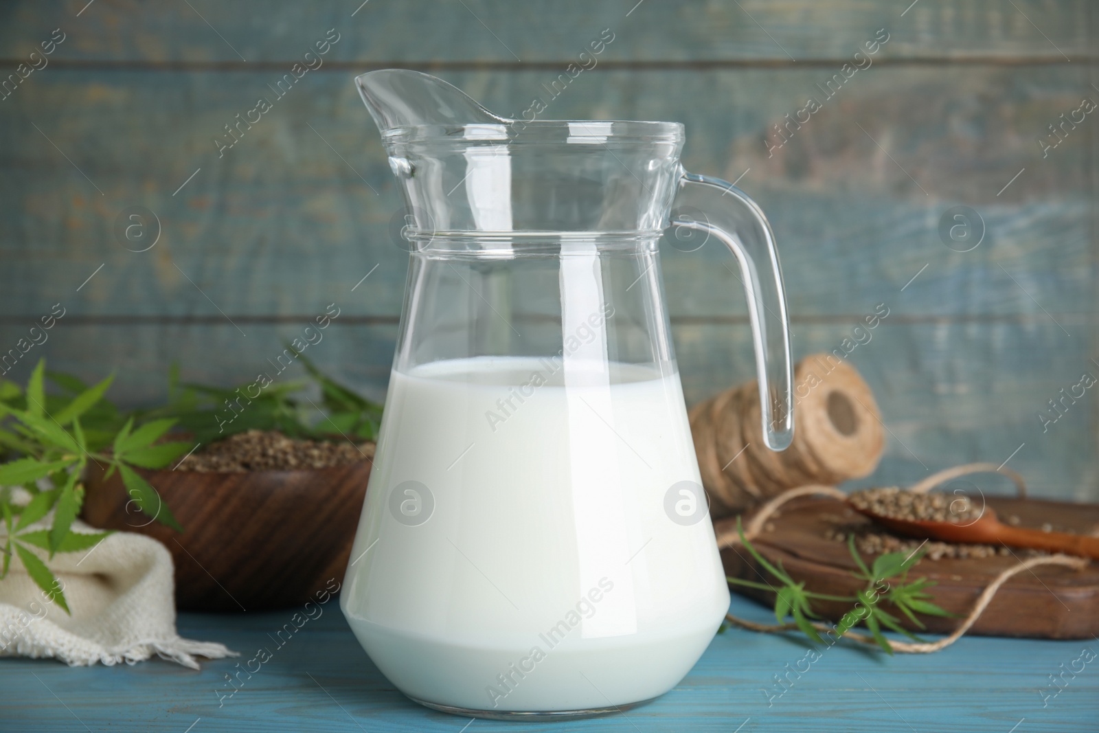 Photo of Pitcher of hemp milk on light blue wooden background