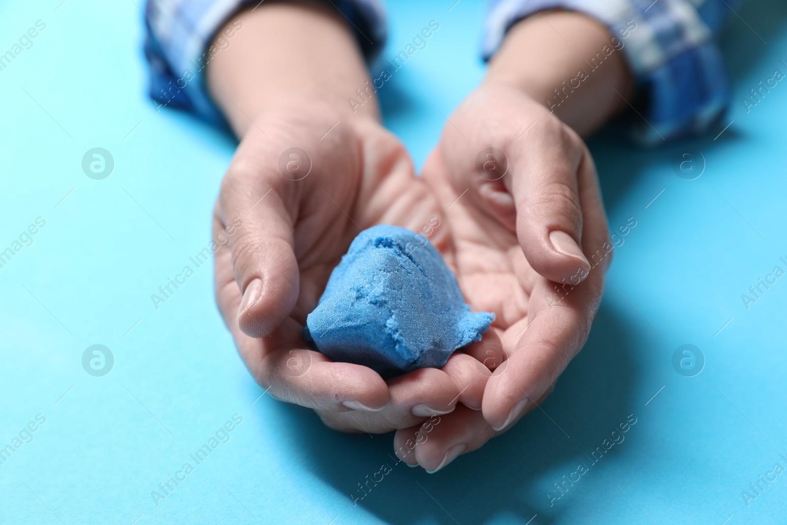 Photo of Woman playing with kinetic sand on light blue background, closeup