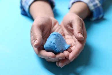 Woman playing with kinetic sand on light blue background, closeup