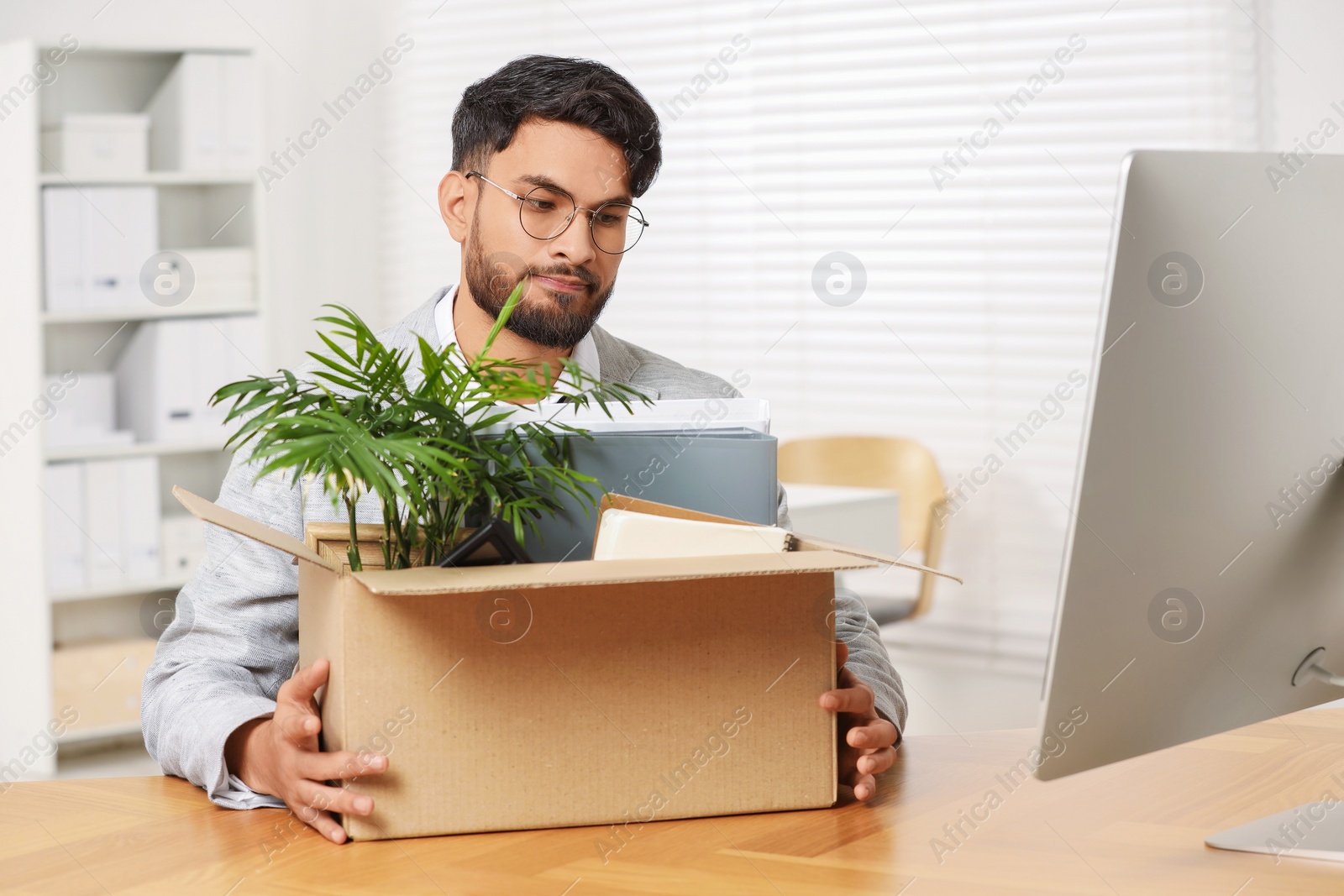 Photo of Unemployment problem. Frustrated man with box of personal belongings at desk in office