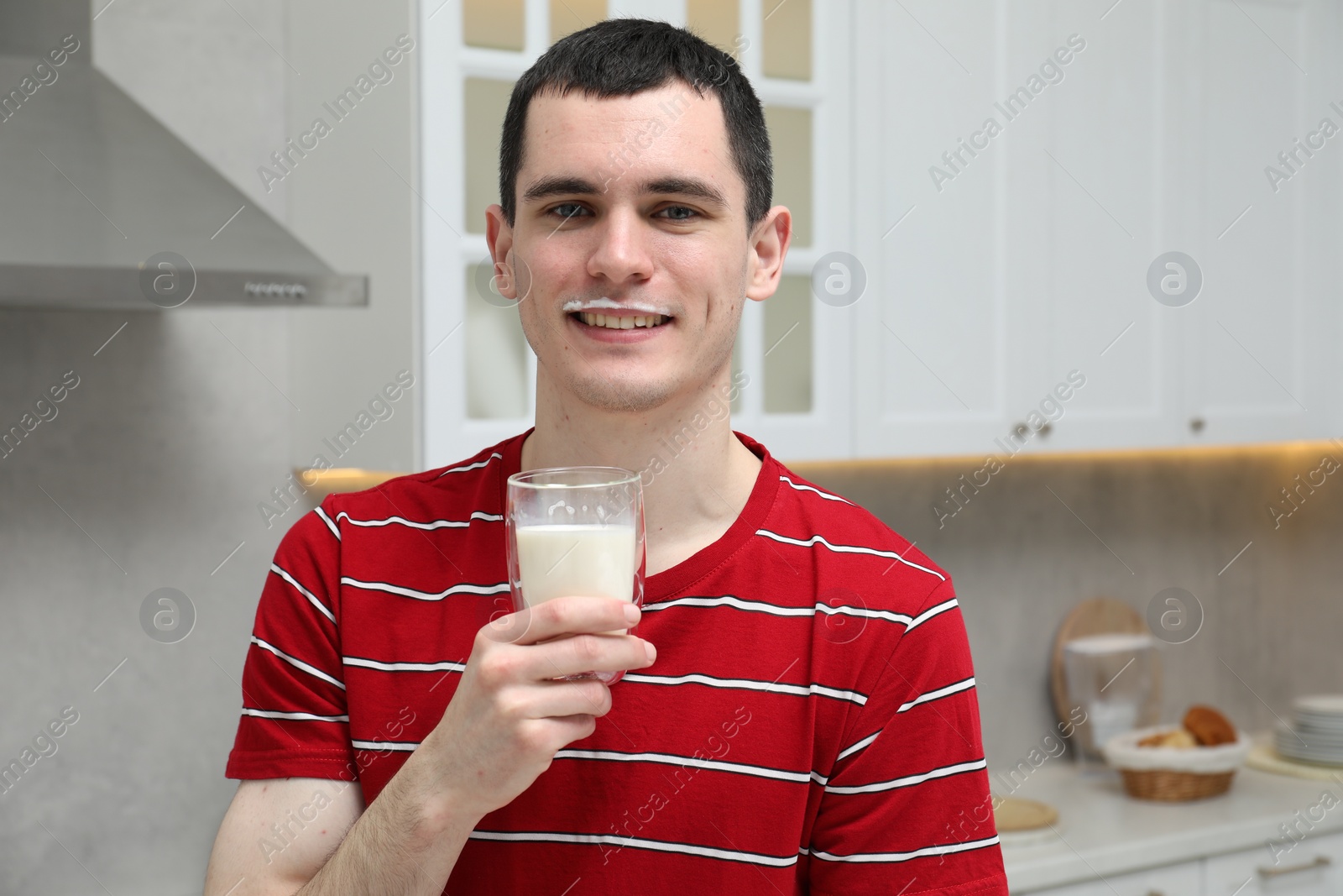Photo of Happy man with milk mustache holding glass of tasty dairy drink in kitchen