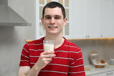 Happy man with milk mustache holding glass of tasty dairy drink in kitchen