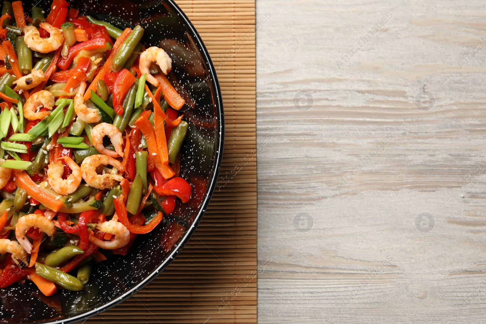 Photo of Shrimp stir fry with vegetables in wok on wooden table, top view. Space for text