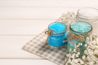 Jars with sea salt and beautiful flowers on white wooden table. Space for text