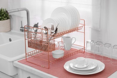 Photo of Drying rack with clean dishes and cutlery on countertop near sink in kitchen