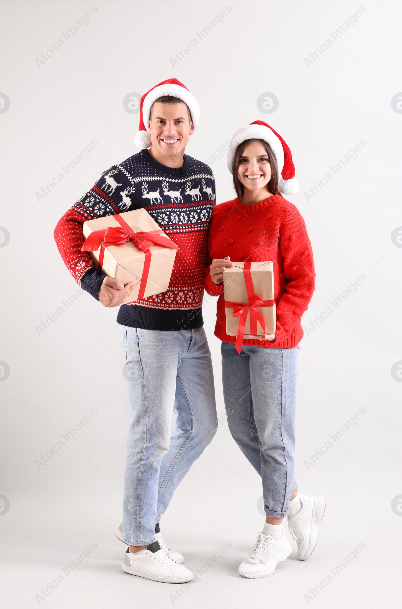 Photo of Beautiful happy couple in Santa hats holding Christmas gifts on light background