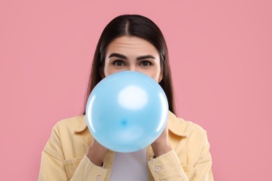 Photo of Woman inflating light blue balloon on pink background