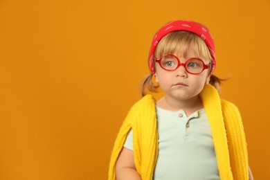 Cute little girl in glasses on orange background. Space for text