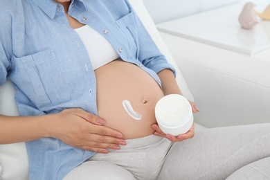 Photo of Pregnant woman applying body cream on belly at home, closeup