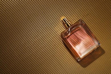 Luxury women's perfume. Sunlit glass bottle on golden surface, top view. Space for text