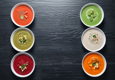 Photo of Various soups in bowls and space for text on wooden background, top view. Healthy food