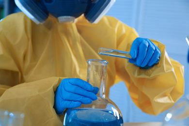 Photo of Scientist in chemical protective suit pouring reagent into flask at laboratory, closeup. Virus research