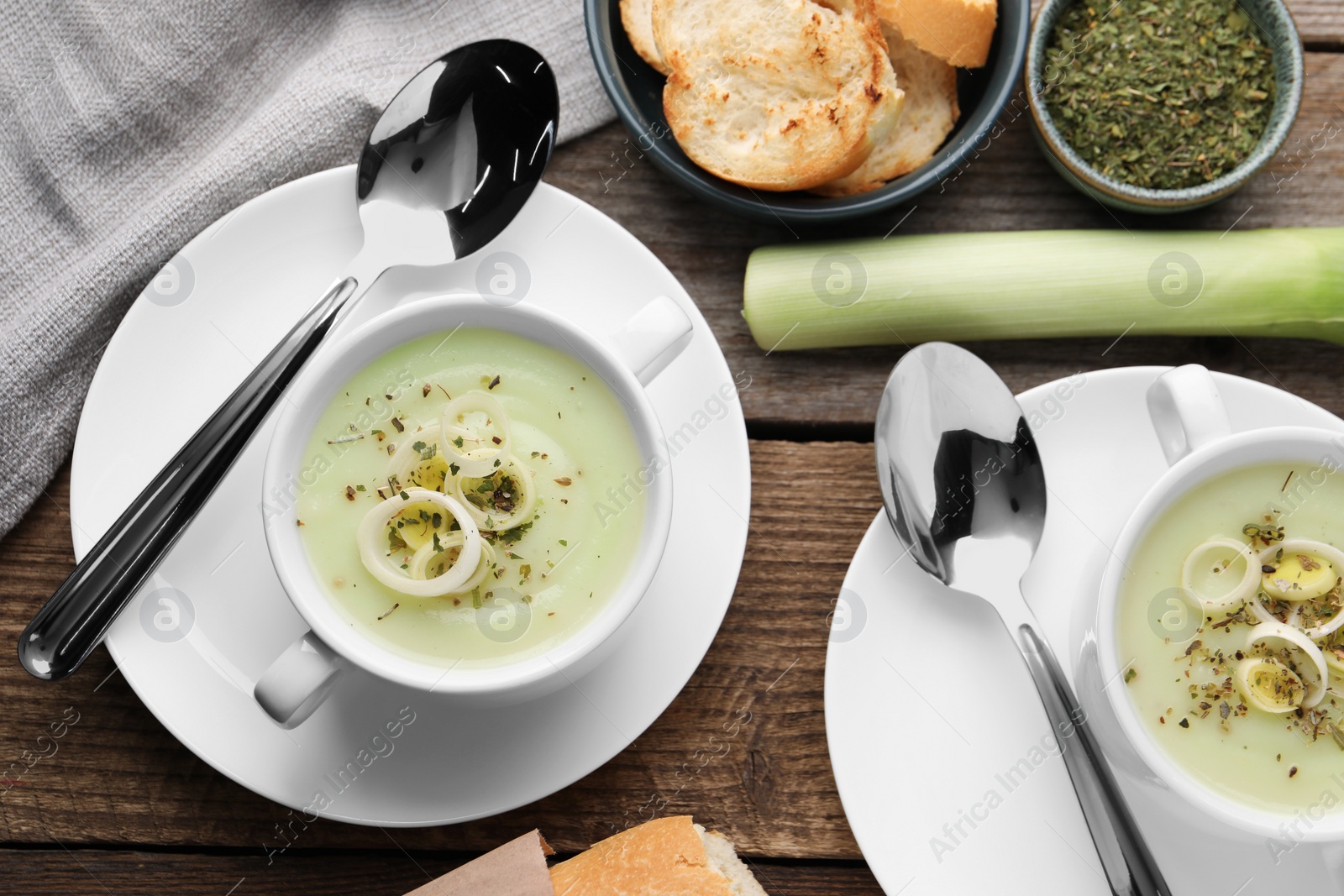 Photo of Delicious cream soup with leek and spices served on wooden table, flat lay