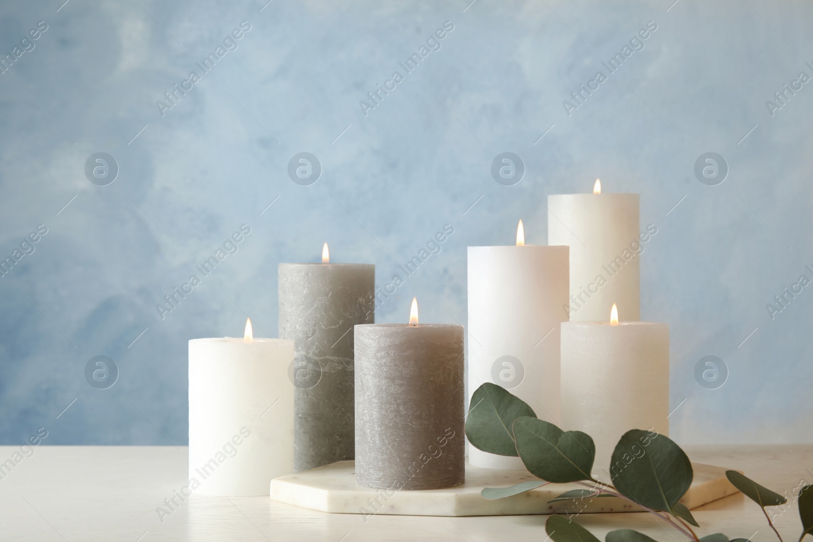 Photo of Composition with burning candles on table against color background