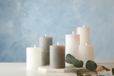 Photo of Composition with burning candles on table against color background