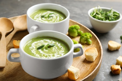 Photo of Bowls of delicious broccoli cream soup with microgreens served on tray