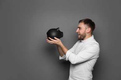 Photo of Young man with piggy bank on grey background. Space for text