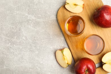 Photo of Delicious cider and ripe red apples on light grey table, flat lay. Space for text
