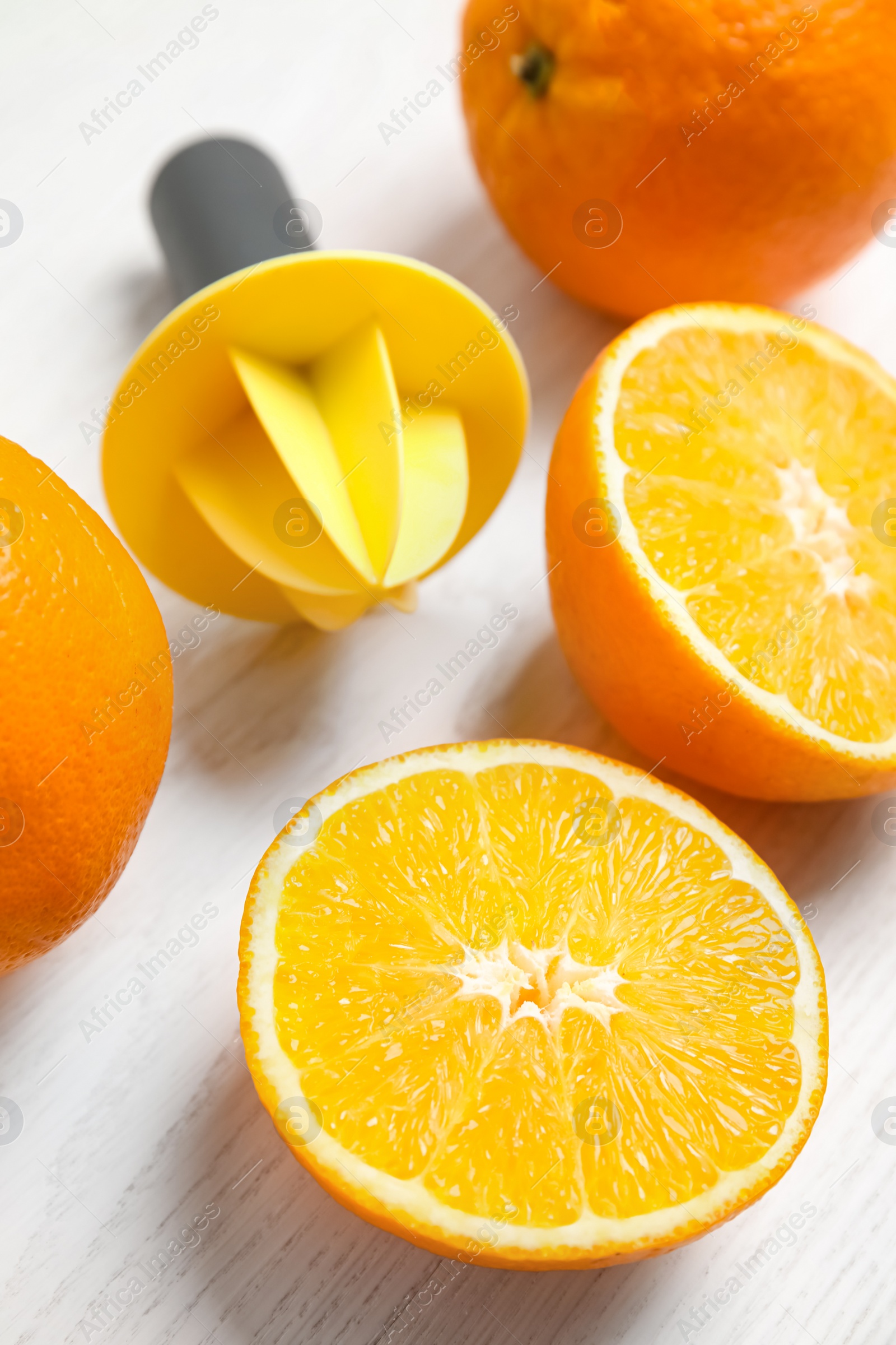 Photo of Fresh ripe oranges and reamer on white wooden table