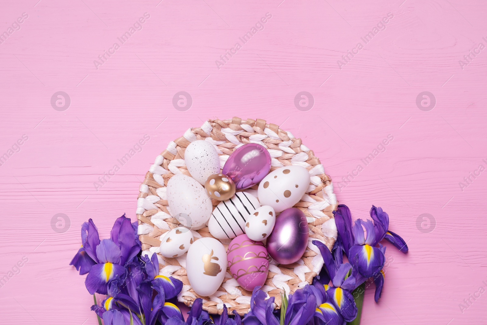 Photo of Flat lay composition with festively decorated Easter eggs and iris flowers on pink wooden background