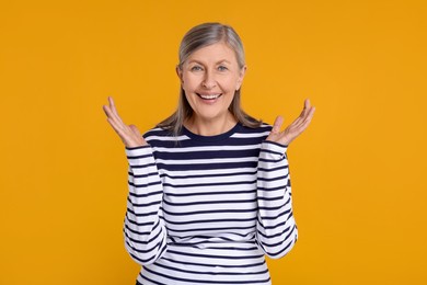 Portrait of happy surprised senior woman on yellow background