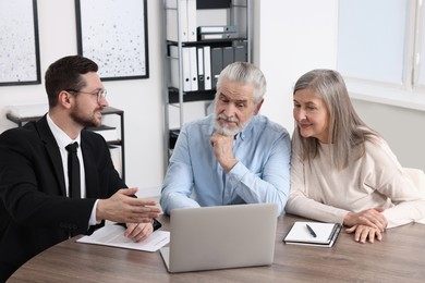 Insurance agent consulting elderly couple about pension plan at wooden table in office